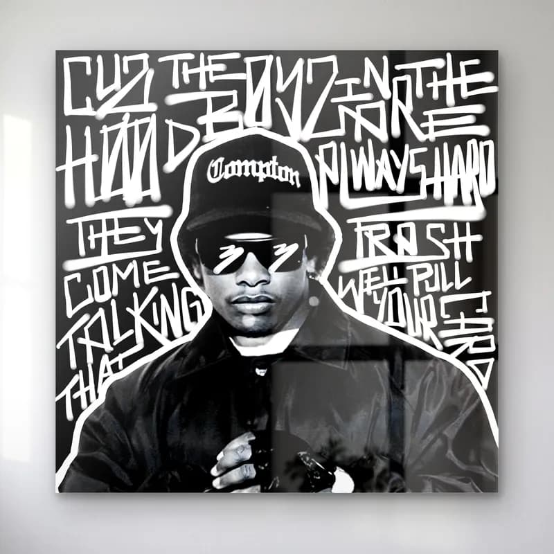 Eazy-E Compton Grafiti cam tablo — Siyah beyaz grafiti yazıları arasında Compton şapkalı ve gözlüklü Eazy-E portresi