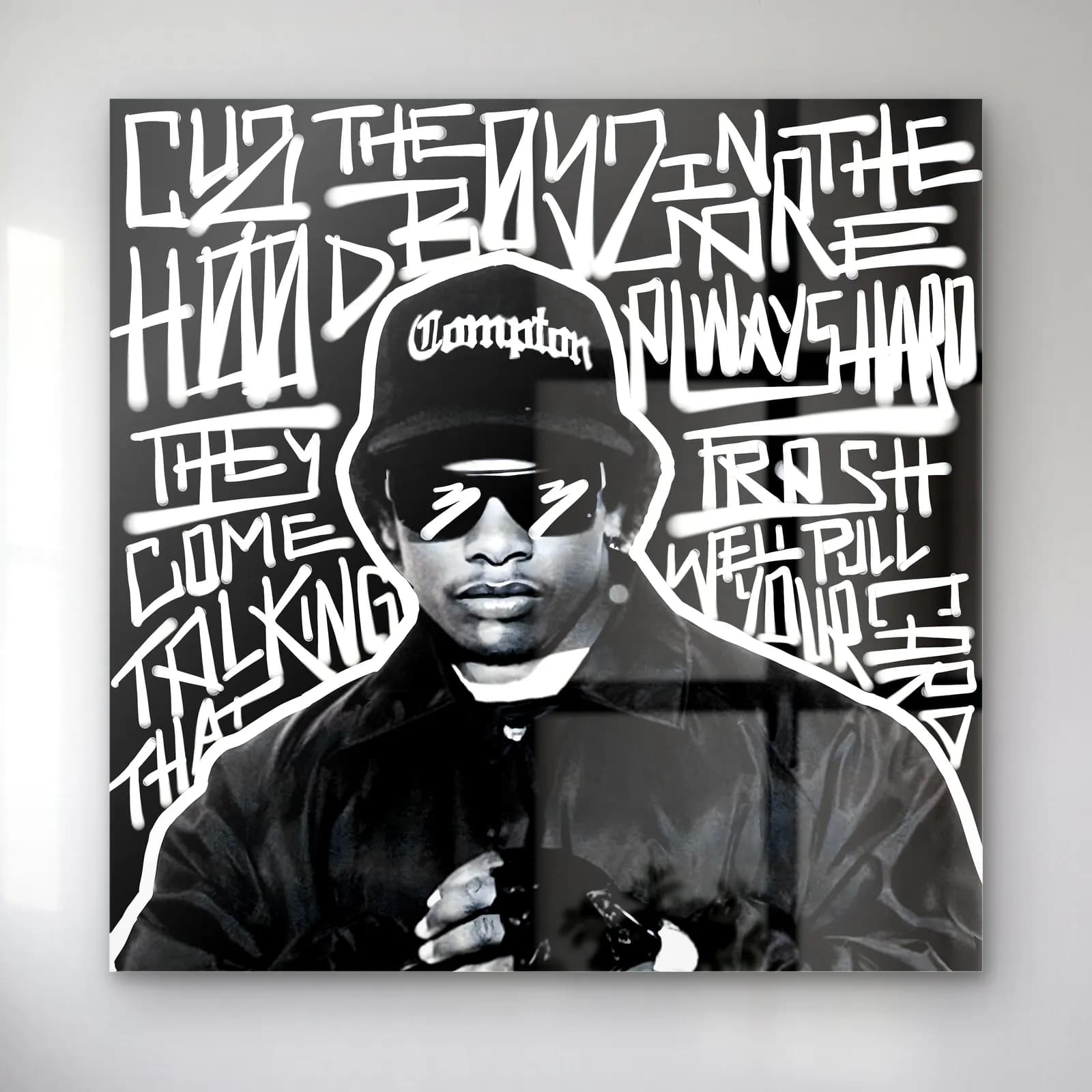 Eazy-E Compton Grafiti cam tablo — Siyah beyaz grafiti yazıları arasında Compton şapkalı ve gözlüklü Eazy-E portresi
